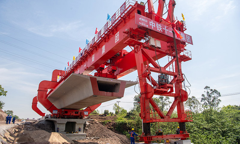 近日，在由中鐵十一局集團(tuán)承建的渝昆高鐵重慶段建設(shè)現(xiàn)場(chǎng)，首榀重約830噸的大型箱梁精準(zhǔn)架設(shè)在金家灣1號(hào)中橋上，標(biāo)志著渝昆高鐵重慶段正式拉開架梁序幕。圖為在渝昆高鐵重慶段建設(shè)現(xiàn)場(chǎng)，架橋機(jī)在進(jìn)行首榀箱梁架設(shè)作業(yè)。
